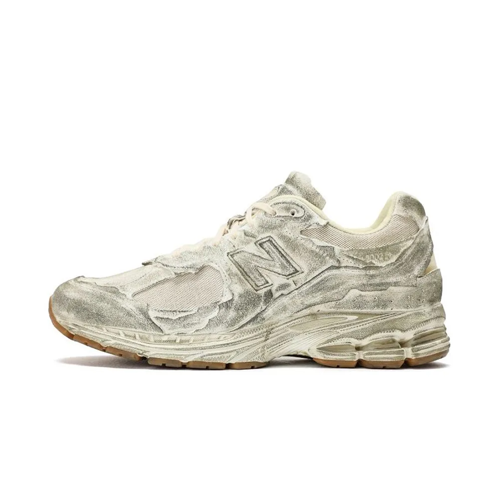 Кроссовки New Balance 2002R Protection Pack Distressed в серо-бежевом цвете. Ракурс сбоку: потертый дизайн с текстурной подошвой и логотипом NB